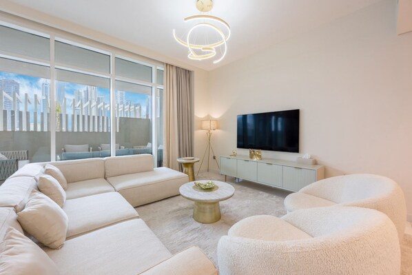 A modern living room with a large sofa, a round coffee table, a TV, and a cityscape view through large windows.