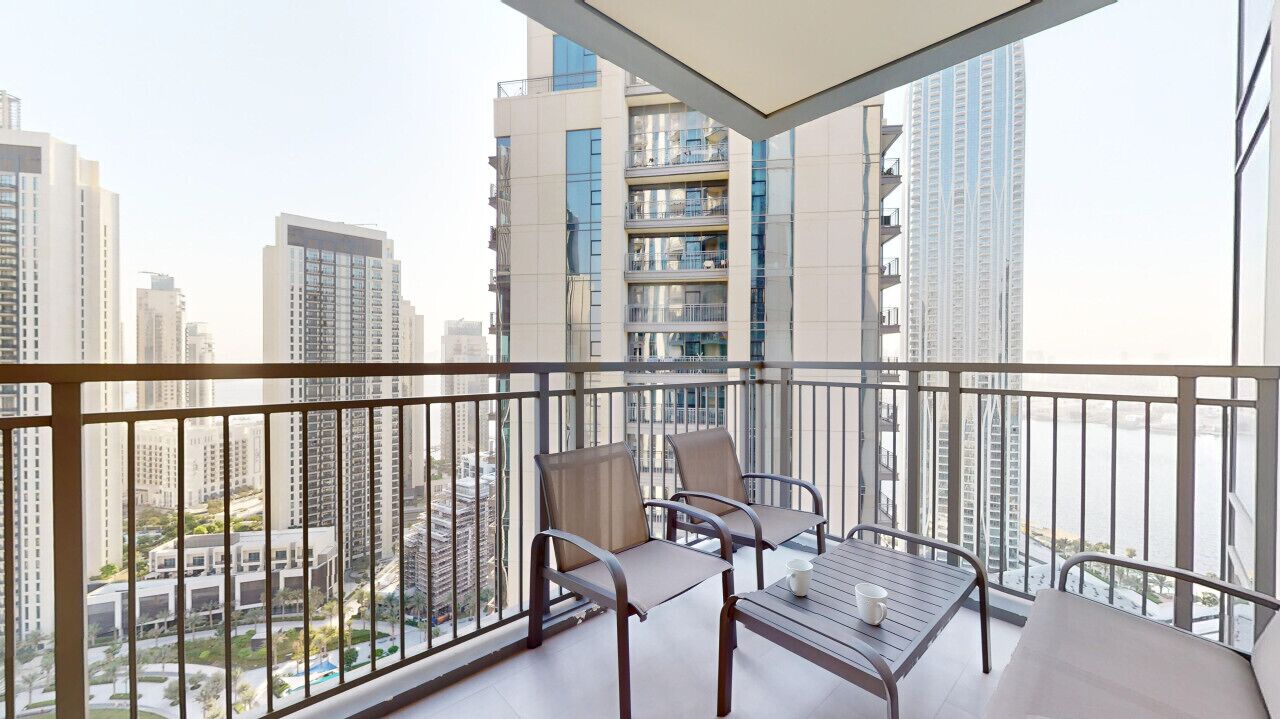 A balcony with a table and chairs, offering a view of high-rise buildings and a cityscape.