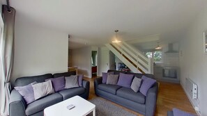 Un salon moderne avec deux canapés gris, une table basse blanche et un escalier menant à la cuisine.