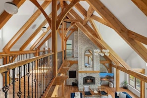 Un loft amplio con vigas de madera a la vista, chimenea de piedra y balcón con barandilla de hierro forjado.