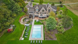 Una casa grande con piscina, rodeada de un césped cuidado y árboles.