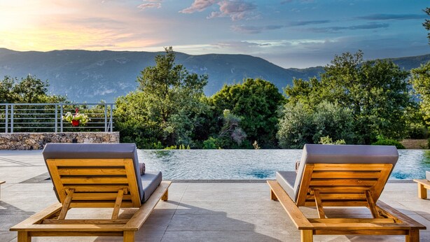 A poolside area with wooden lounge chairs and a view of mountains.