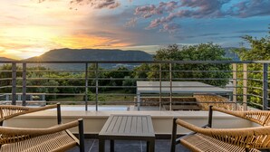 A balcony with wicker chairs, a table, and a view of mountains and greenery.