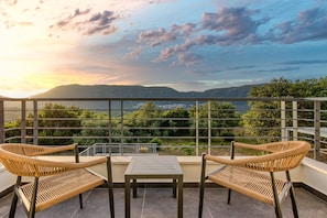 A balcony with wicker chairs and a table, overlooking a scenic landscape with mountains and greenery. - Villa Sunset Bliss| private pool - country views (Corfu)