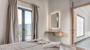 A bedroom with a large bed, a bedside mirror, and a view of the outdoors.
