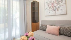 A room with a grey sofa, a pink pillow, a glass cabinet, and a floral artwork on the wall. - Bethy's #1|Double BR Apt (Corfu)