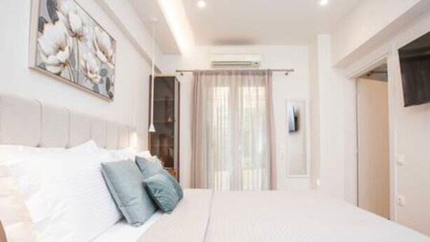 A bedroom with a large bed, a headboard, a wall-mounted air conditioner, and a door with a curtain. - Bethy's #1|Double BR Apt (Corfu)