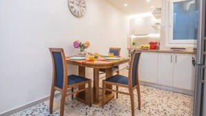 A dining area with a round table, two chairs, a clock on the wall, and a kitchen in the background. - Bethy's #1|Double BR Apt (Corfu)