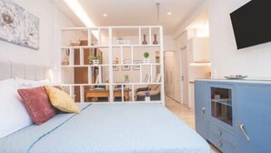 A bedroom with a bed, a wardrobe, a television, and a white shelving unit.