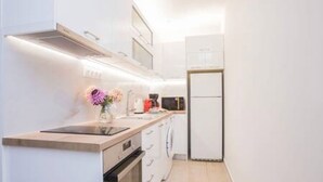 A modern kitchen with white cabinetry, a built-in oven, and a stainless steel refrigerator.