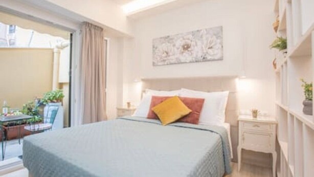 A bedroom with a bed, a nightstand, a wall-mounted shelf with plants, and a painting.