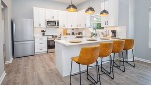 Une cuisine moderne avec des meubles blancs, un réfrigérateur en acier inoxydable, un four à micro-ondes et un grand îlot central doté de tabourets de bar.