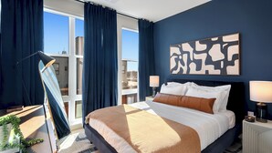 A modern hotel room with a large bed, a desk, and a view of the city. - Luxury 2BR Apt + Work-From-Home Space (New Haven)
