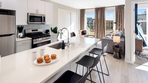 A modern kitchen with a central island, stainless steel appliances, and a dining area with black chairs. - Luxury 2BR Apt + Work-From-Home Space (New Haven)