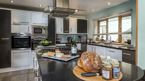 A modern kitchen with stainless steel appliances, a marble countertop, and a large island with food items and a loaf of bread.