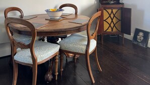 Un coin repas comprenant une table ronde en bois, quatre chaises rembourrées, un saladier rempli de fruits et un téléviseur fixé au mur.