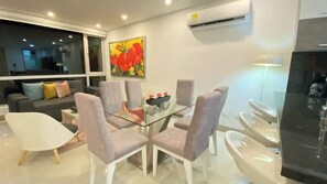 A modern dining area with a glass table and cushioned chairs, a sofa with pillows, and a painting on the wall. - Nice 3BR condo w/ ocean view (Cartagena de Indias)