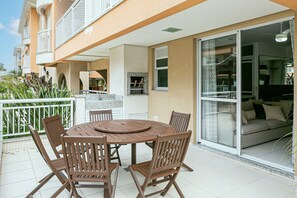 Een balkon met een ronde houten tafel en stoelen, een glazen deur naar een woonruimte, en een witte balustrade.
