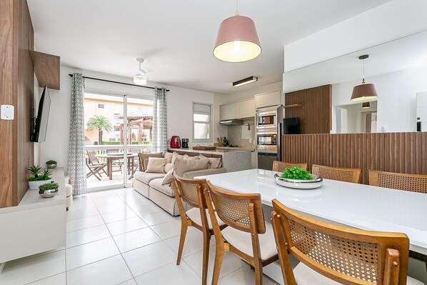 Een moderne keuken met een eethoek, met een wit aanrecht, houten stoelen en een groot raam.