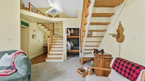 Amplia sala de estar con techo alto, escalera de madera, una cama litera y un rincón de descanso acogedor.
