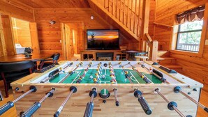 A wooden-floored room with a foosball table, a television, and a dining table.