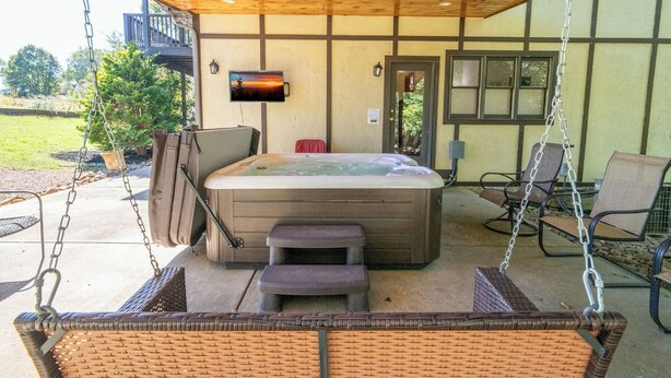 Un bain à remous installé sous une pergola en bois, avec des fauteuils en osier et une balançoire.