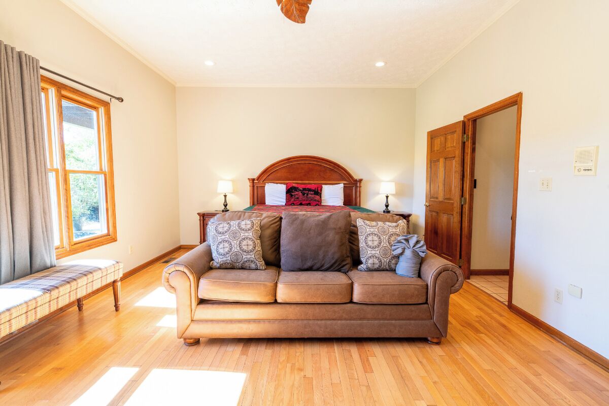 A cozy room with a wooden floor, a brown sofa with patterned cushions, a wooden headboard, and two bedside lamps.
