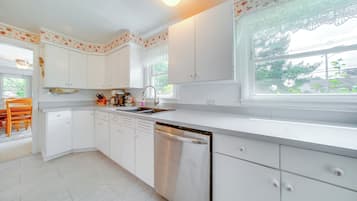 Une cuisine moderne avec des meubles blancs, un lave-vaisselle et une fenêtre donnant sur un espace verdoyant.