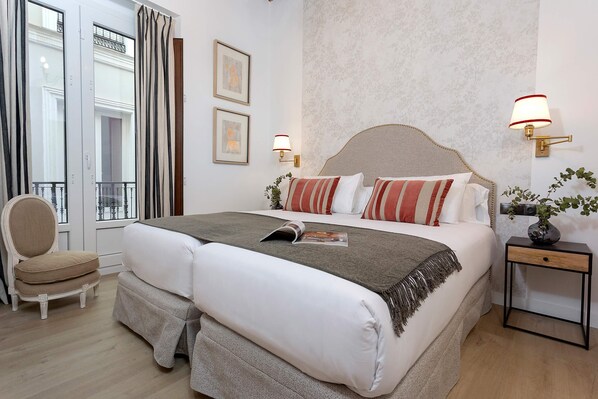 Una habitación de hotel con una cama grande, dos mesitas de noche, una silla y una ventana con cortinas.