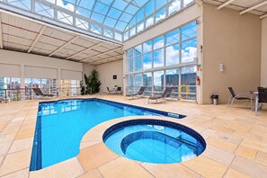 Una piscina interior con techo de vidrio, sillones de descanso y vista a la ciudad.