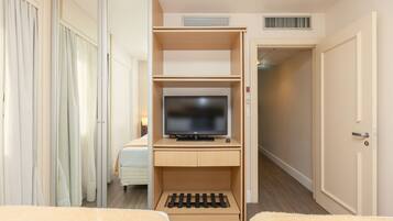 A hotel room with a TV on a wooden shelf, a bed, and a door to a hallway.