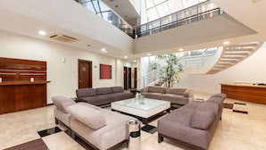 Un vestíbulo espacioso con techo alto, una zona de estar central con sofás, una recepción y una escalera que lleva a un nivel superior.