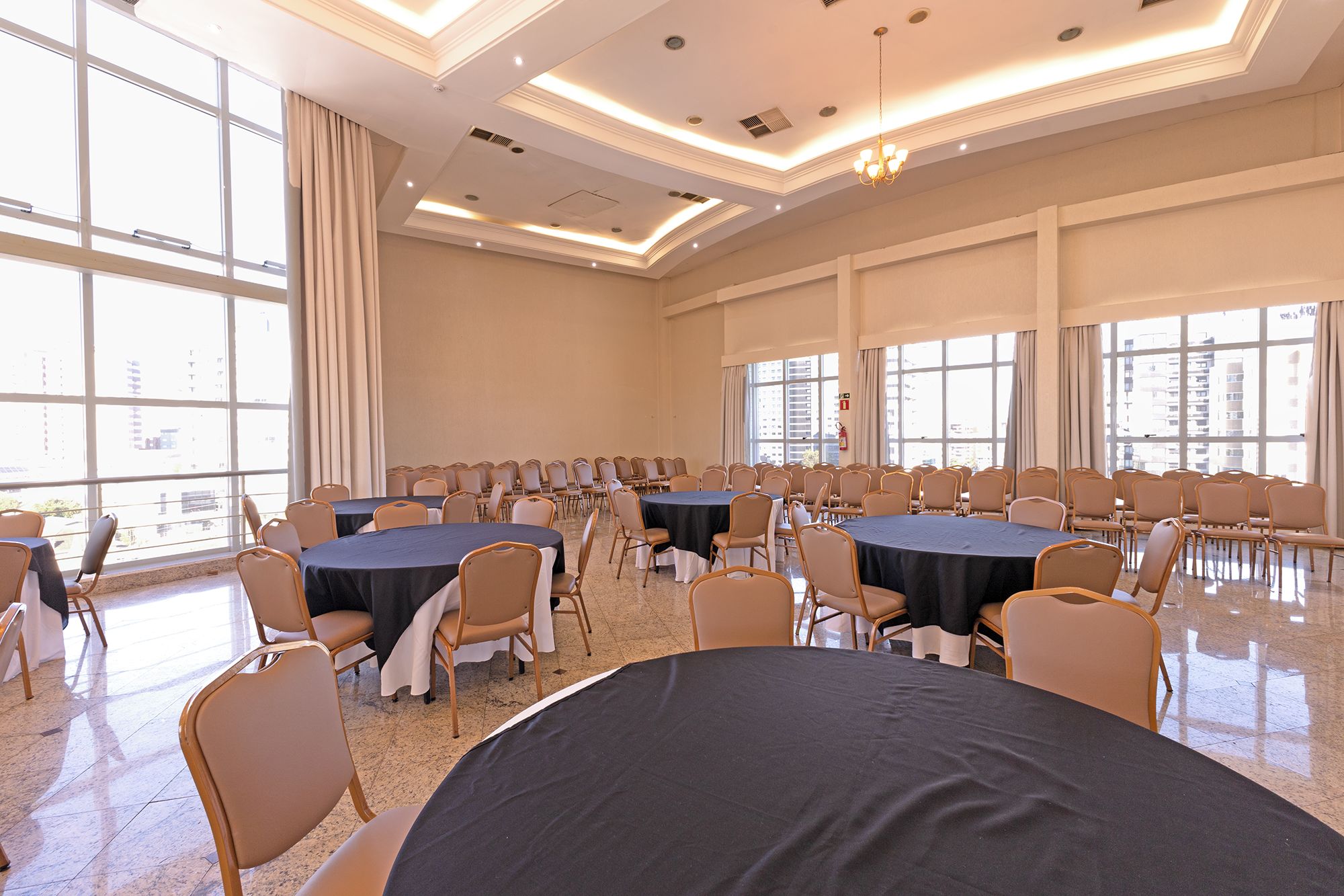 A conference room with multiple round tables, chairs, and large windows allowing natural light.