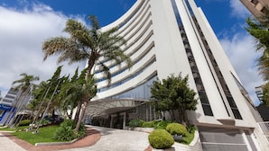 Un edificio moderno con fachada curva, acceso cubierto y vegetación circundante.
