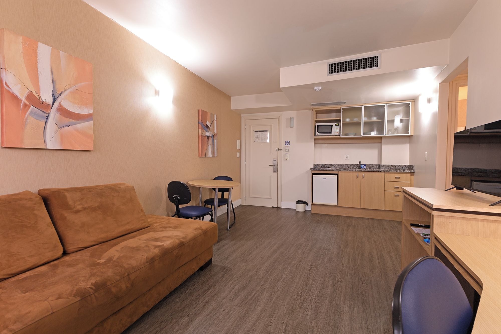 A compact living space with a sofa, a small dining table, a kitchenette, and a television.