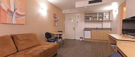 A compact living space with a sofa, a small dining table, a kitchenette, and a television.