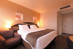 Habitación de hotel con cama, una silla, dos lámparas de pared y obras de arte en las paredes.