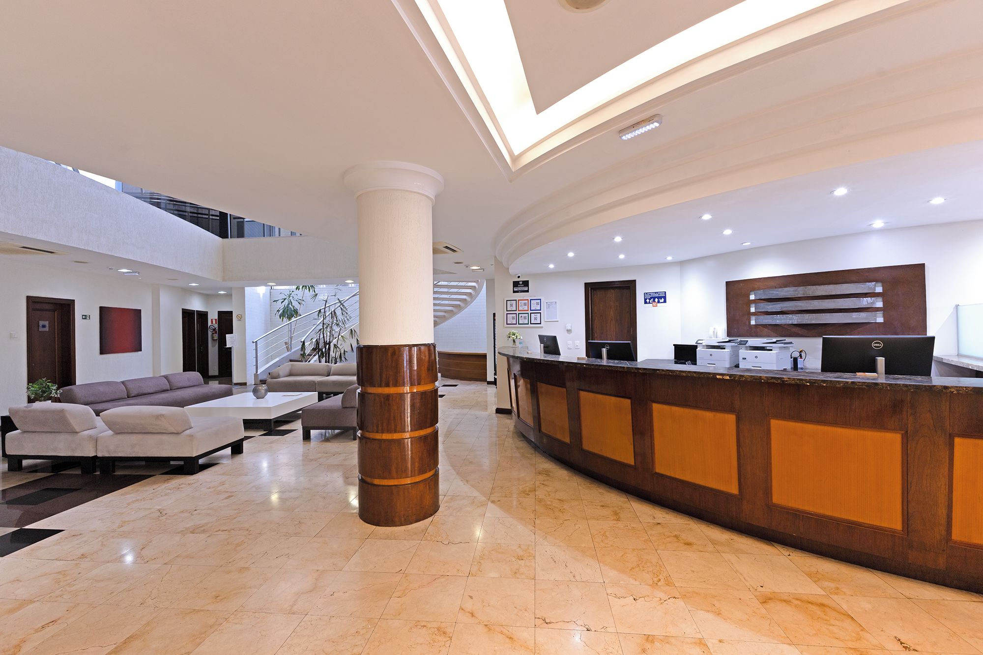 A modern hotel lobby with a reception desk, seating area, and a staircase.