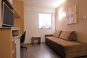 Un espacio habitable pequeño con un sofá, una televisión, una mesita y un ventanal.