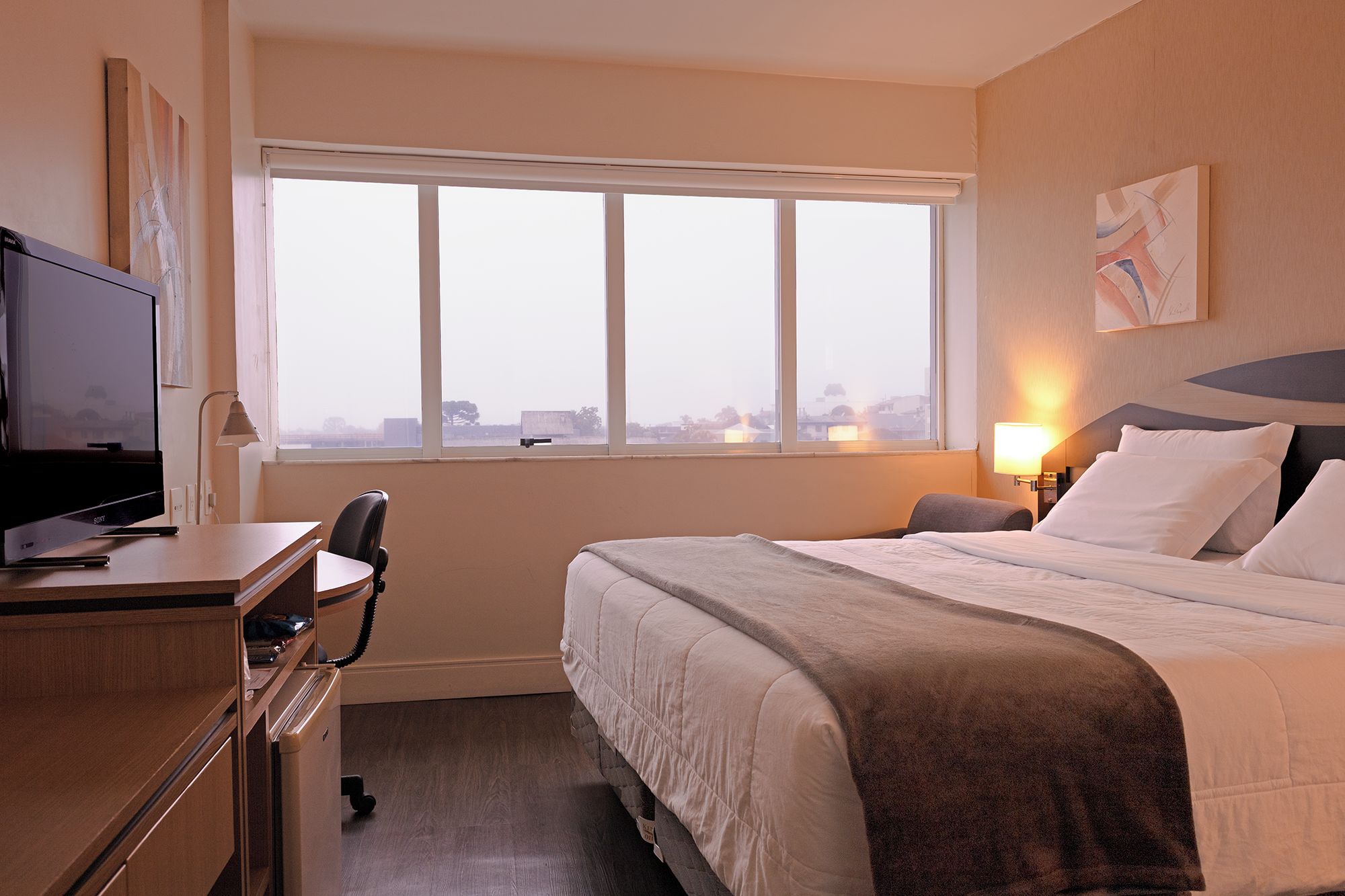 Habitación de hotel con cama, escritorio con computadora, silla y ventana con vistas.