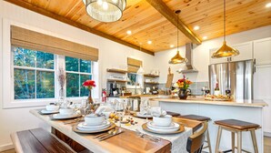 A modern kitchen with wooden beams, stainless steel appliances, and a large dining table set for six. - Luxe Retreat: Sleeps 16, Hot Tub, Sauna & Movie Room (Bethel)