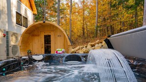 A hot tub area with a wooden structure, a water feature, and a stone wall. - Luxe Retreat: Sleeps 16, Hot Tub, Sauna & Movie Room (Bethel)
