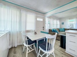 Una habitación compacta y bien iluminada con una mesa de comedor y sillas, un sofá y una pequeña cocina.