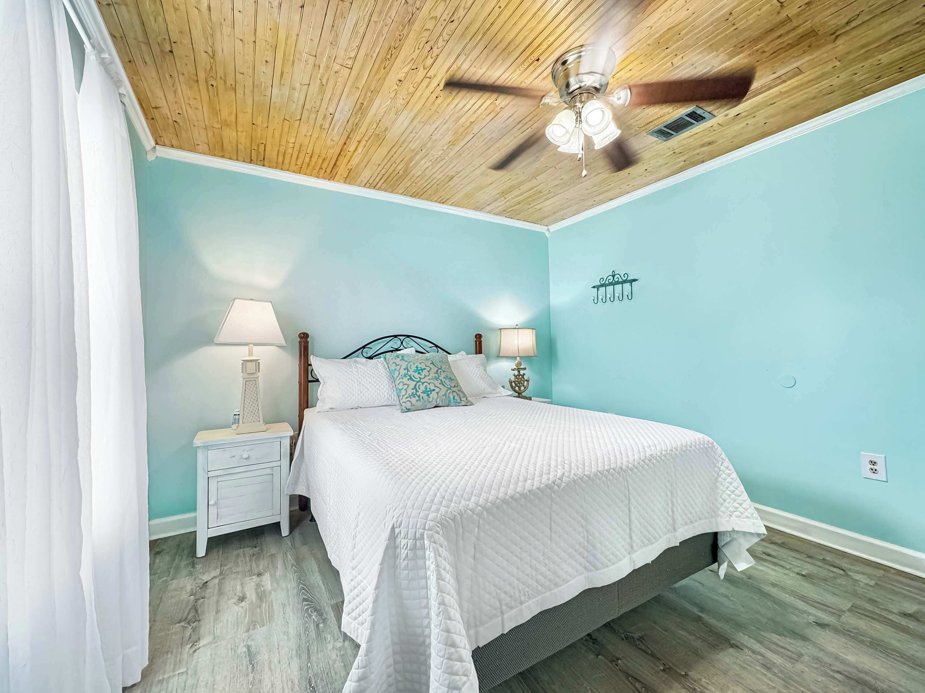 A bedroom with a wooden ceiling, a bed with white bedding, two bedside tables with lamps, and a wall-mounted light fixture.