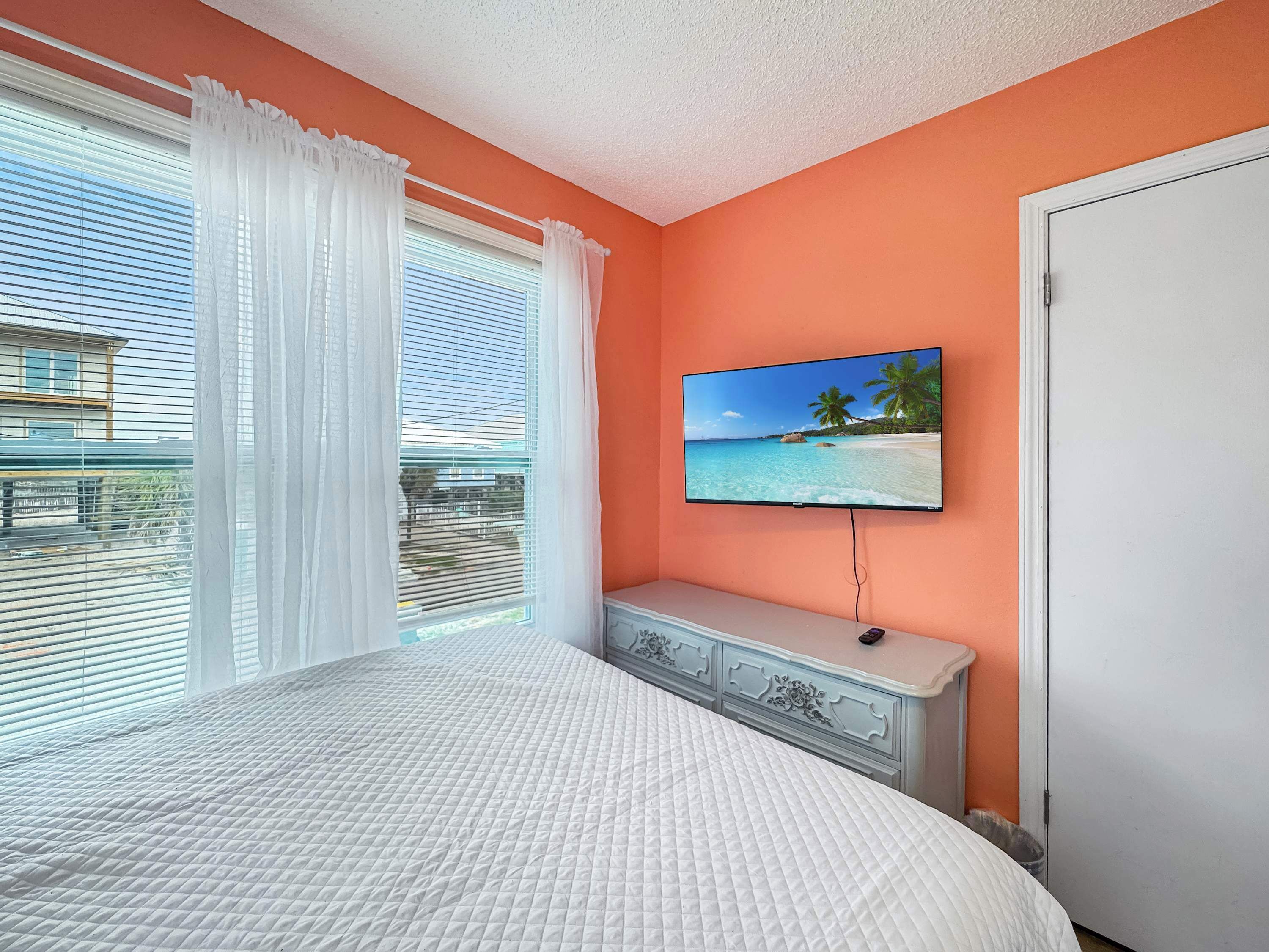 A bedroom with a bed, a TV on the wall, and a window with curtains.