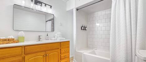 A modern bathroom with a wooden vanity, a large mirror, a white bathtub, and a shower curtain.