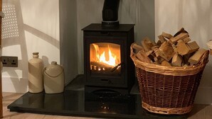 A fireplace with a black wood-burning stove, a mirror above it, and a wooden mantel shelf with decorative items. - Woodview - Idyllic Cottage in the Country (Kinnettles)