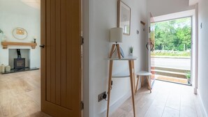 A modern interior with a wooden door, a fireplace, a small table with a lamp, and a view of greenery outside. - Woodview - Idyllic Cottage in the Country (Kinnettles)