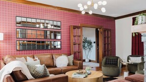 A living room with a brown leather sofa, a round wooden coffee table, and a green armchair. There are multiple mirrors on the wall and a potted plant in the corner. - Hoosier Memories! Luxury Stay, Steps from IU - Pool Table, Firepit & More (Bloomington)