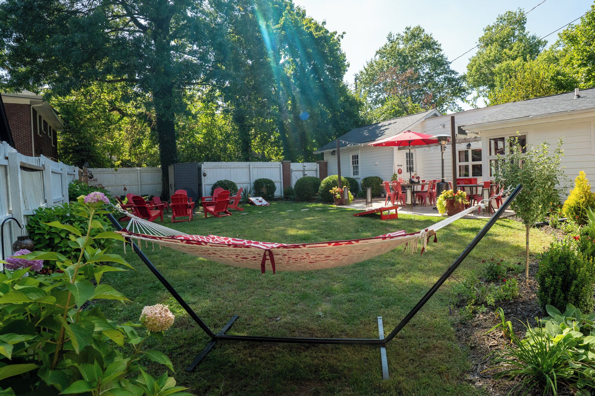 A backyard with a hammock, red chairs, and a dining area with a red umbrella.
